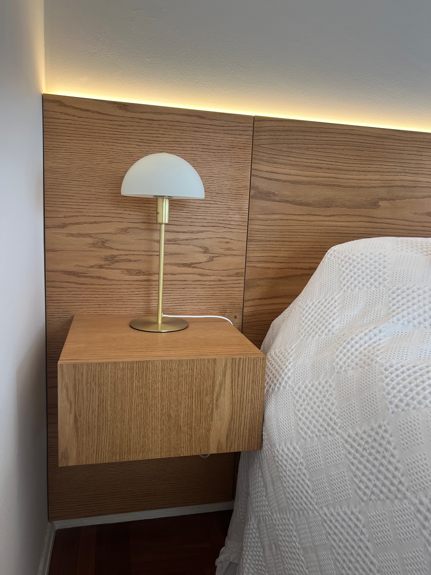 Dormitorio con respaldo de roble, luz indirecta y mesa de luz flotante