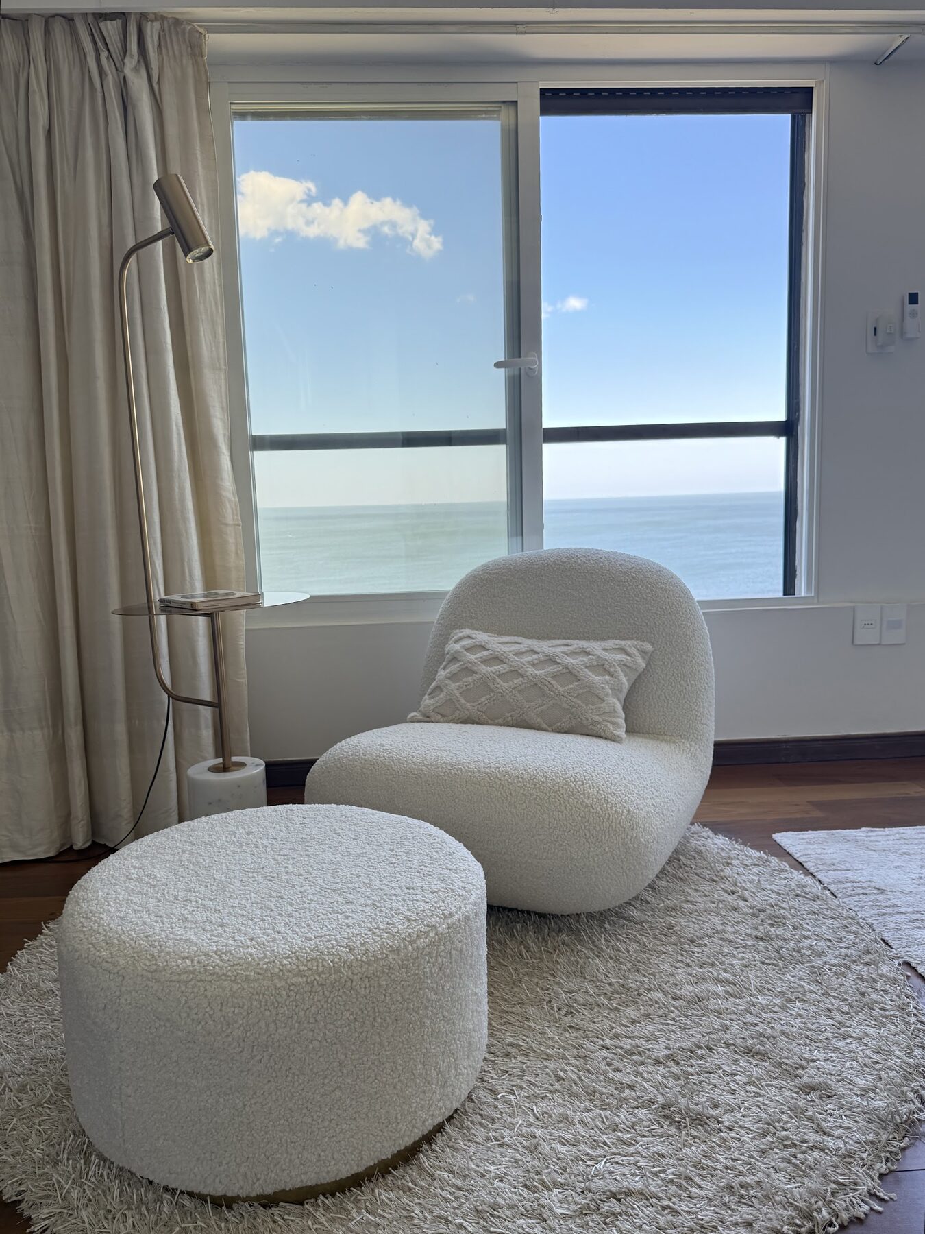 Reforma Rambla Gandhi, bouclé armchair and pouf by the window with a sea view